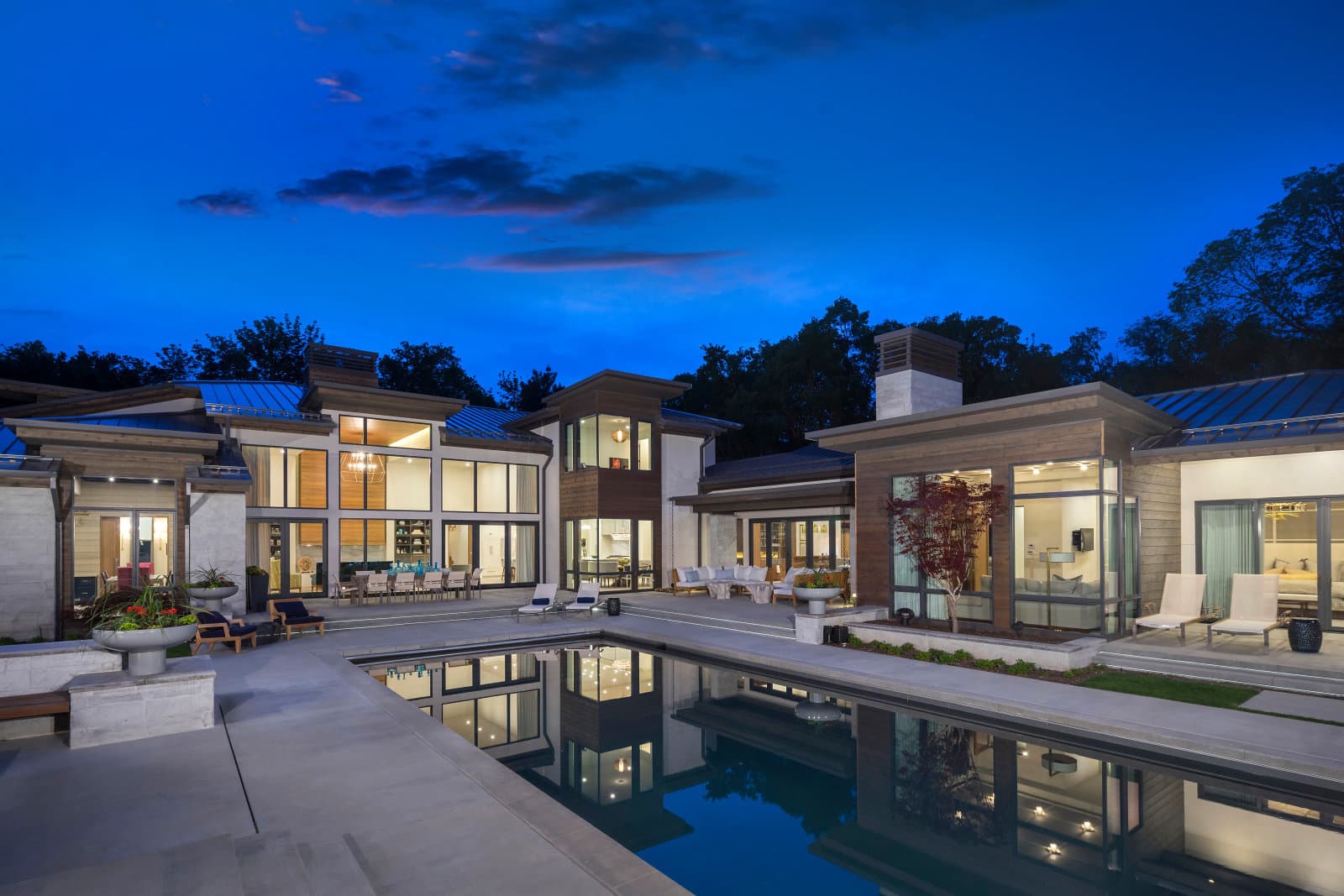 Big Rock rectangular reflecting pool at blue hour with contemporary multi-wing estate and lit poolside lounge in Holladay, Utah