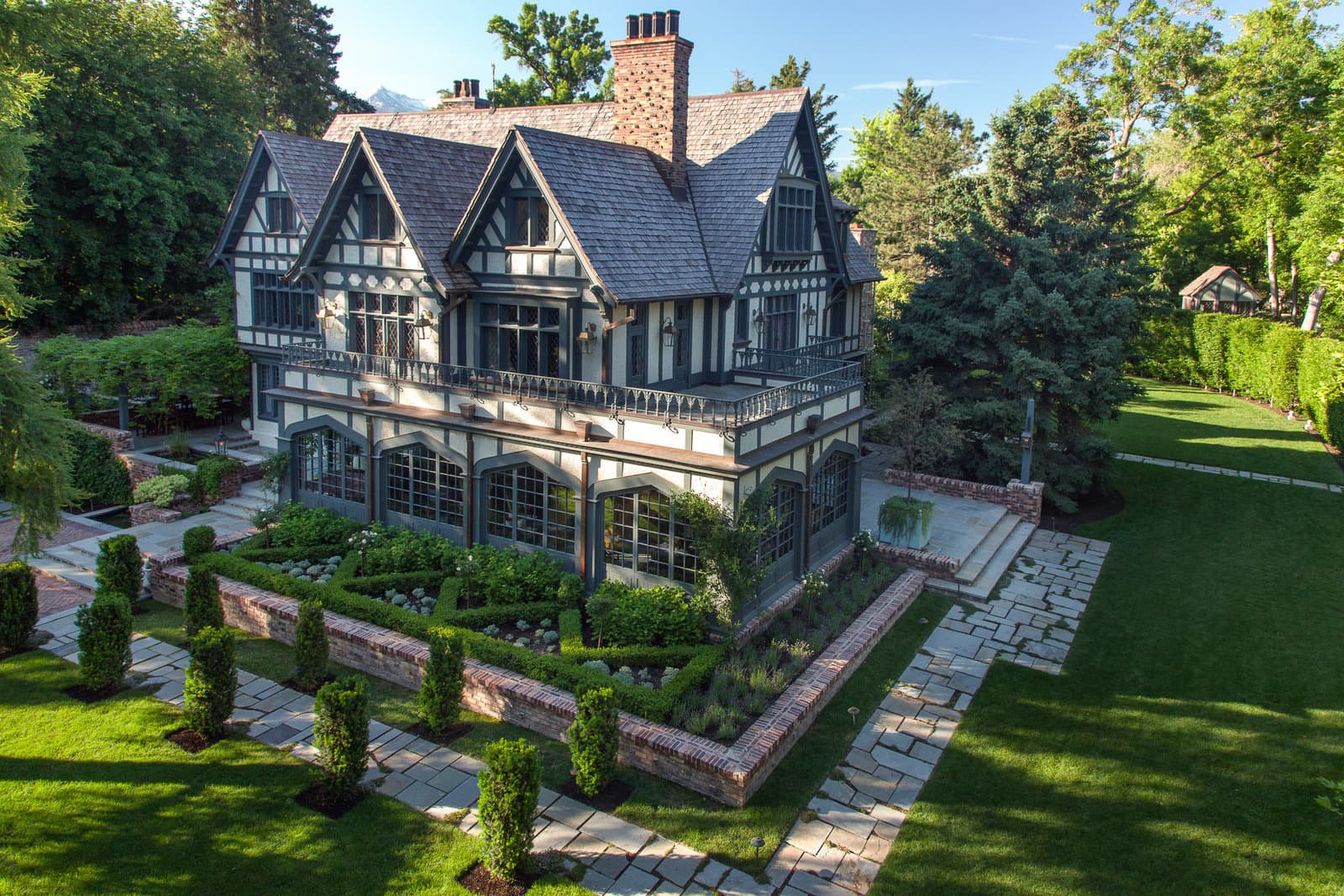 Big Rock Tudor estate with tiered stone retaining walls, flagstone walks, clipped hedges, and mature canopy in Holladay, Utah