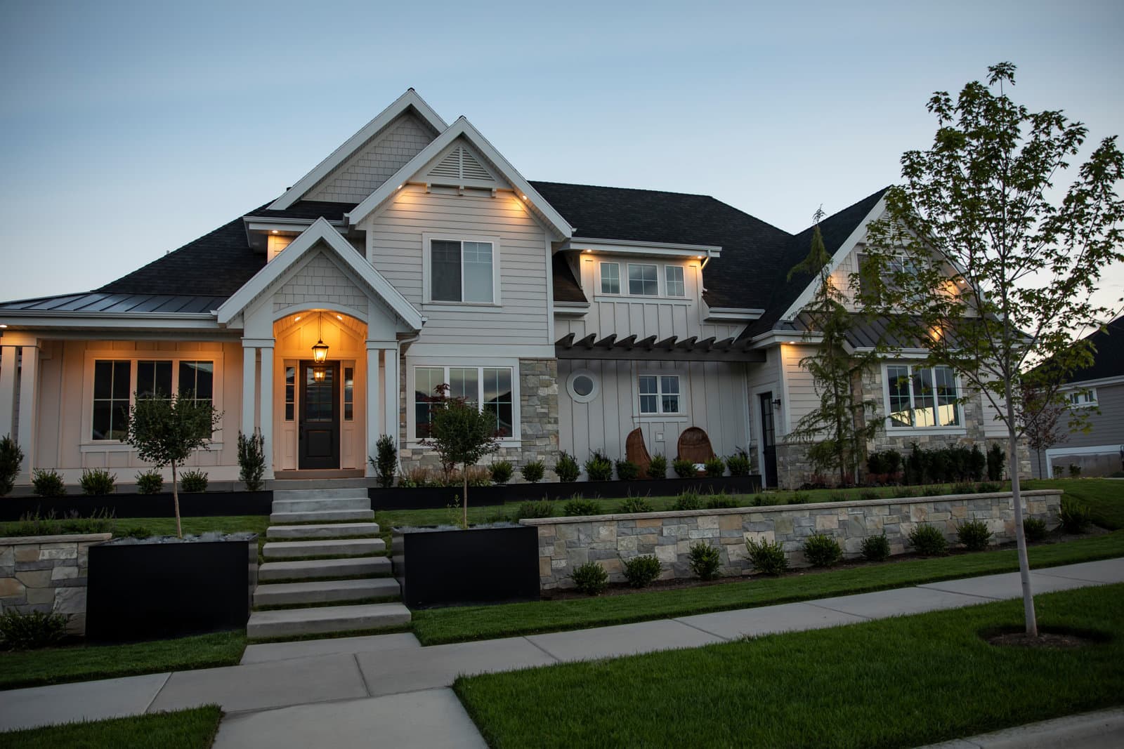 Big Rock traditional Mapleton landscape install with fresh plantings, stone retaining wall, graded lawn, and entry lighting at dusk