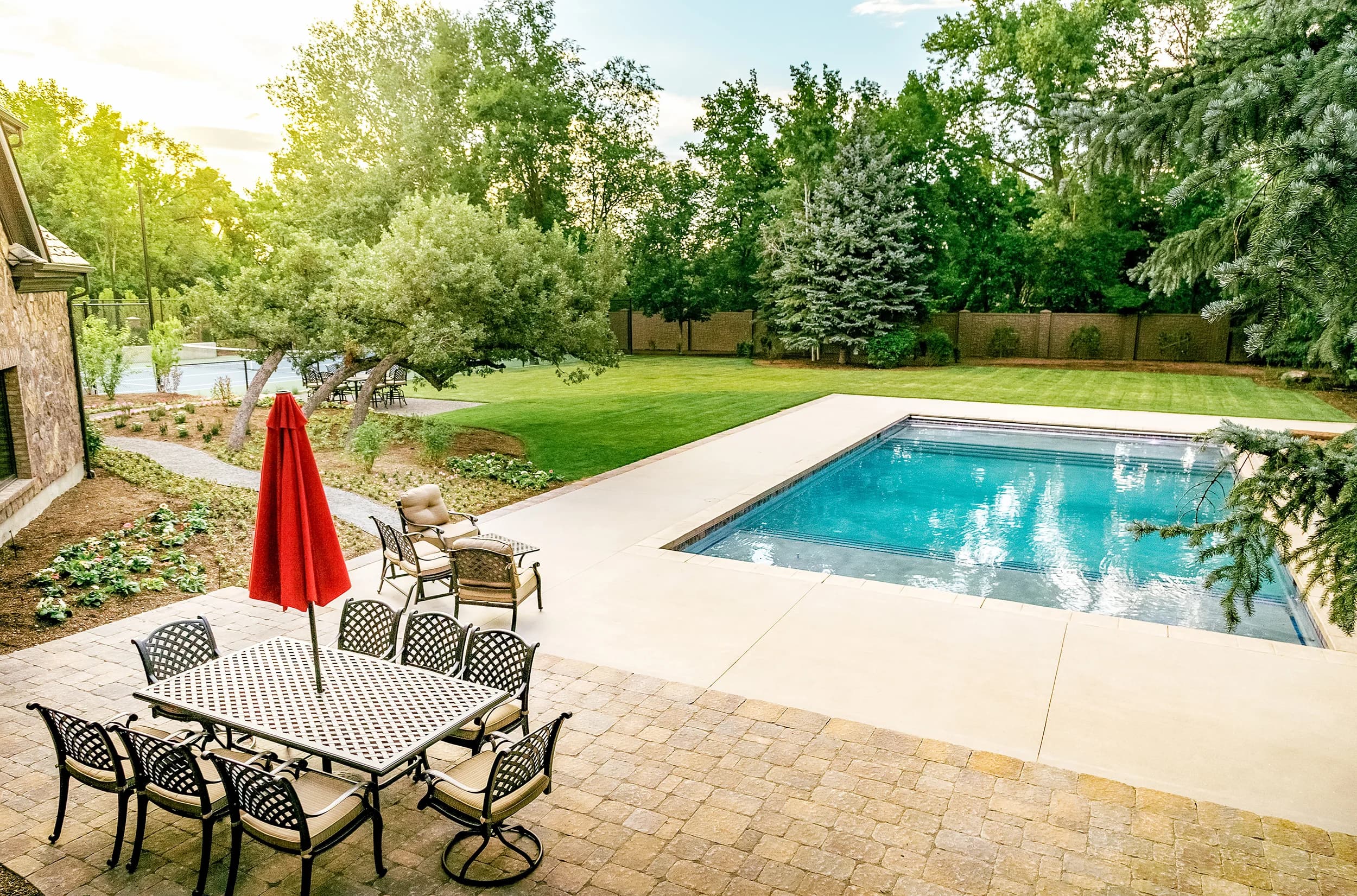 Big Rock custom backyard pool at golden hour with poolside dining, lawn, and family-friendly patio at a Wasatch Front estate