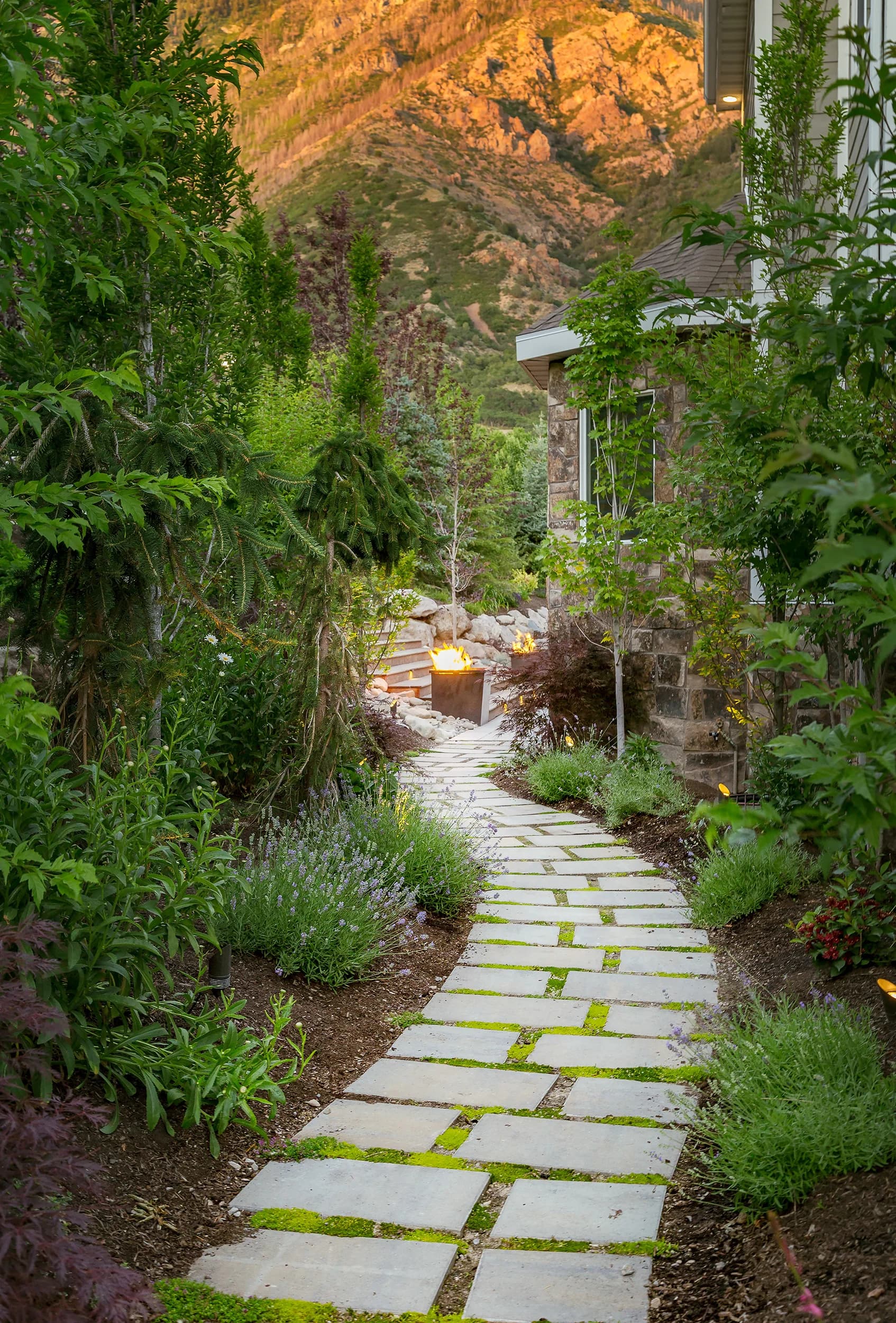 Stone path leading to a fire feature with layered plantings and Wasatch Front mountains at golden hour