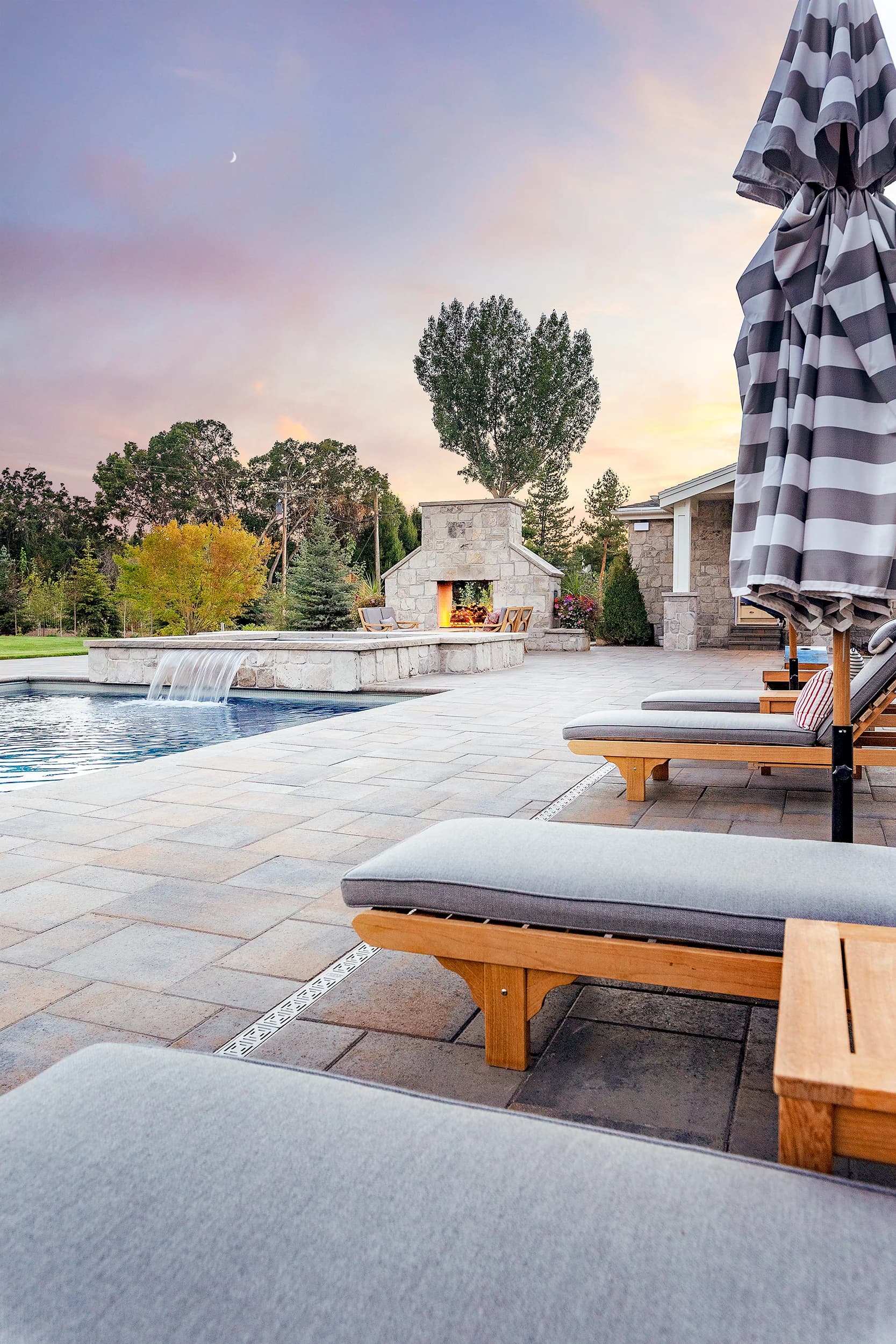 Pool deck chaise lounges leading to a stone fireplace pavilion at sunset on a Big Rock Provo estate