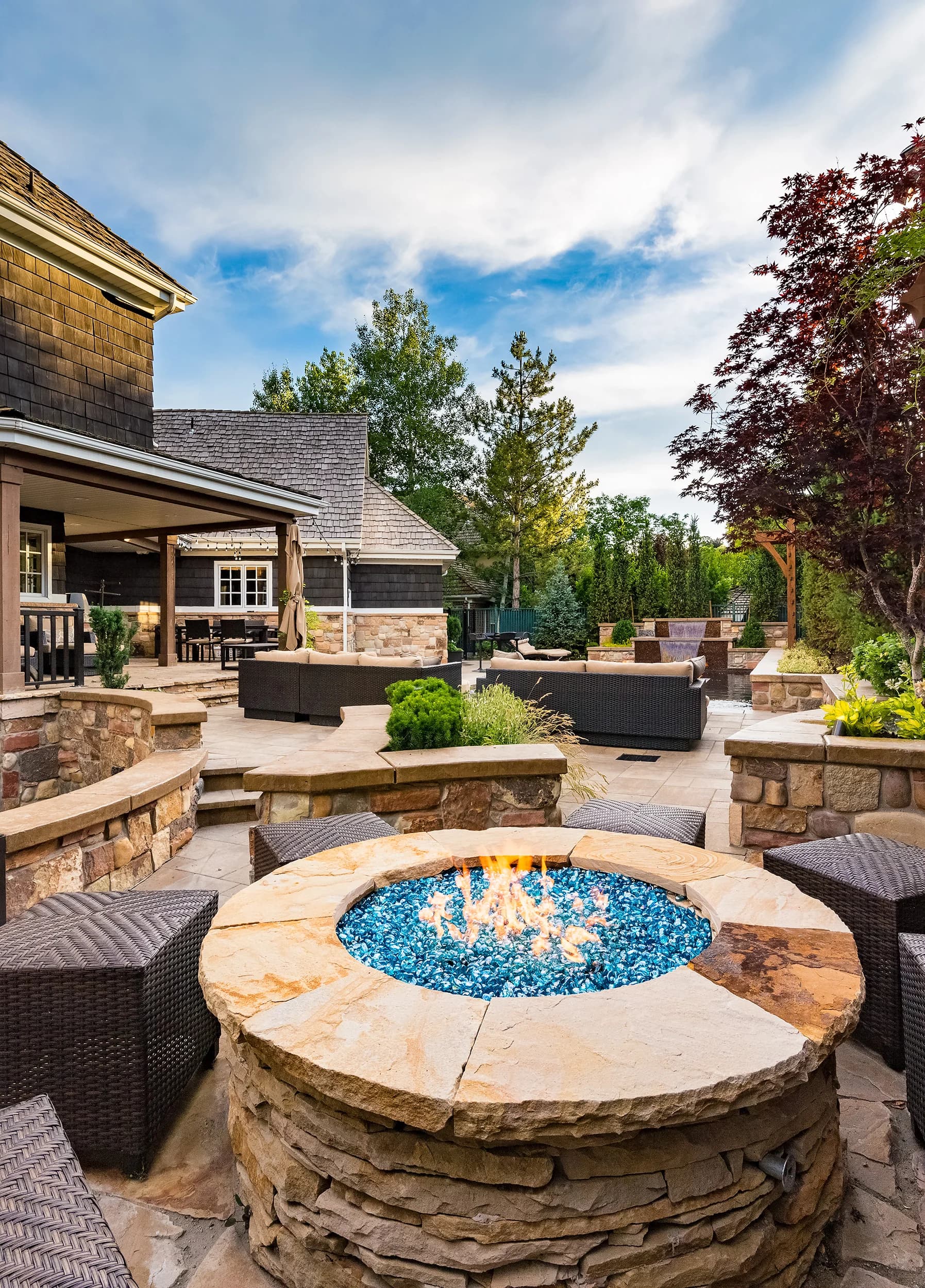Round stone firepit with cobalt fire-glass, flagstone seating, and mature plantings at a Big Rock estate