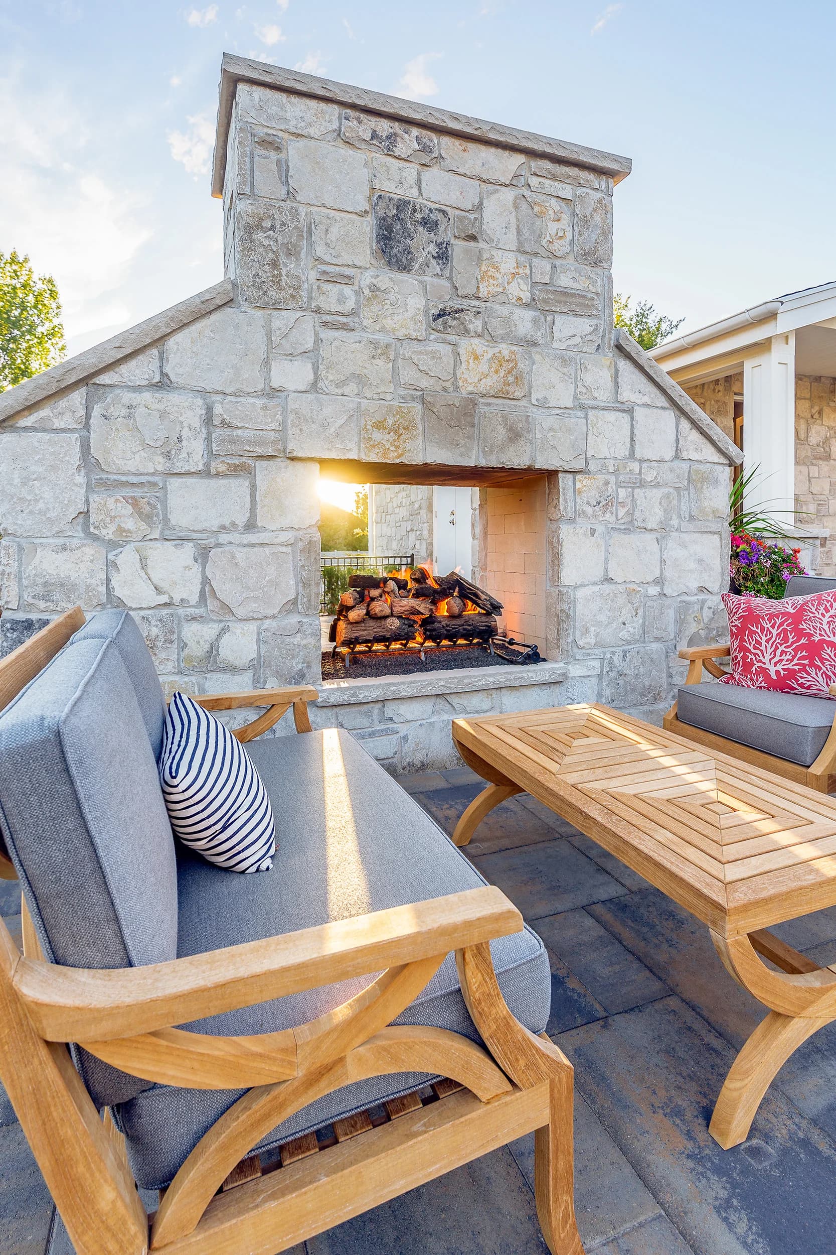 Stone outdoor fireplace with teak seating, blue cushions, and golden hour light at a Big Rock property