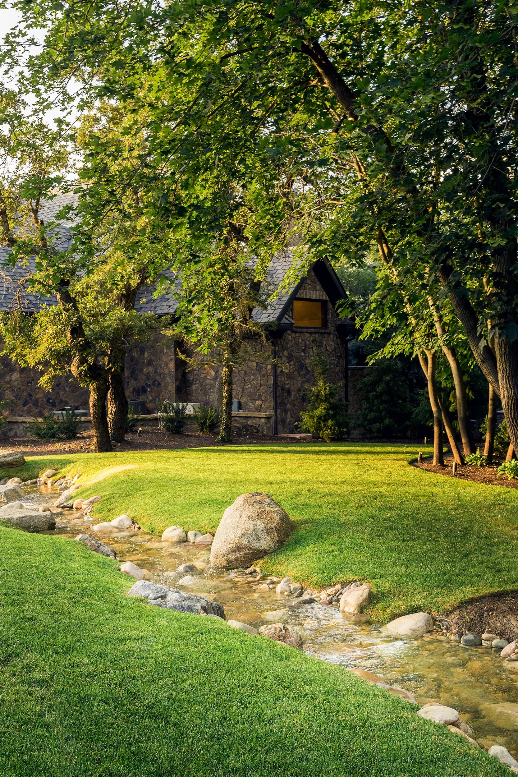 Naturalistic stream and hand-set boulder water feature beside a stone cabin on a Big Rock Wasatch Front property