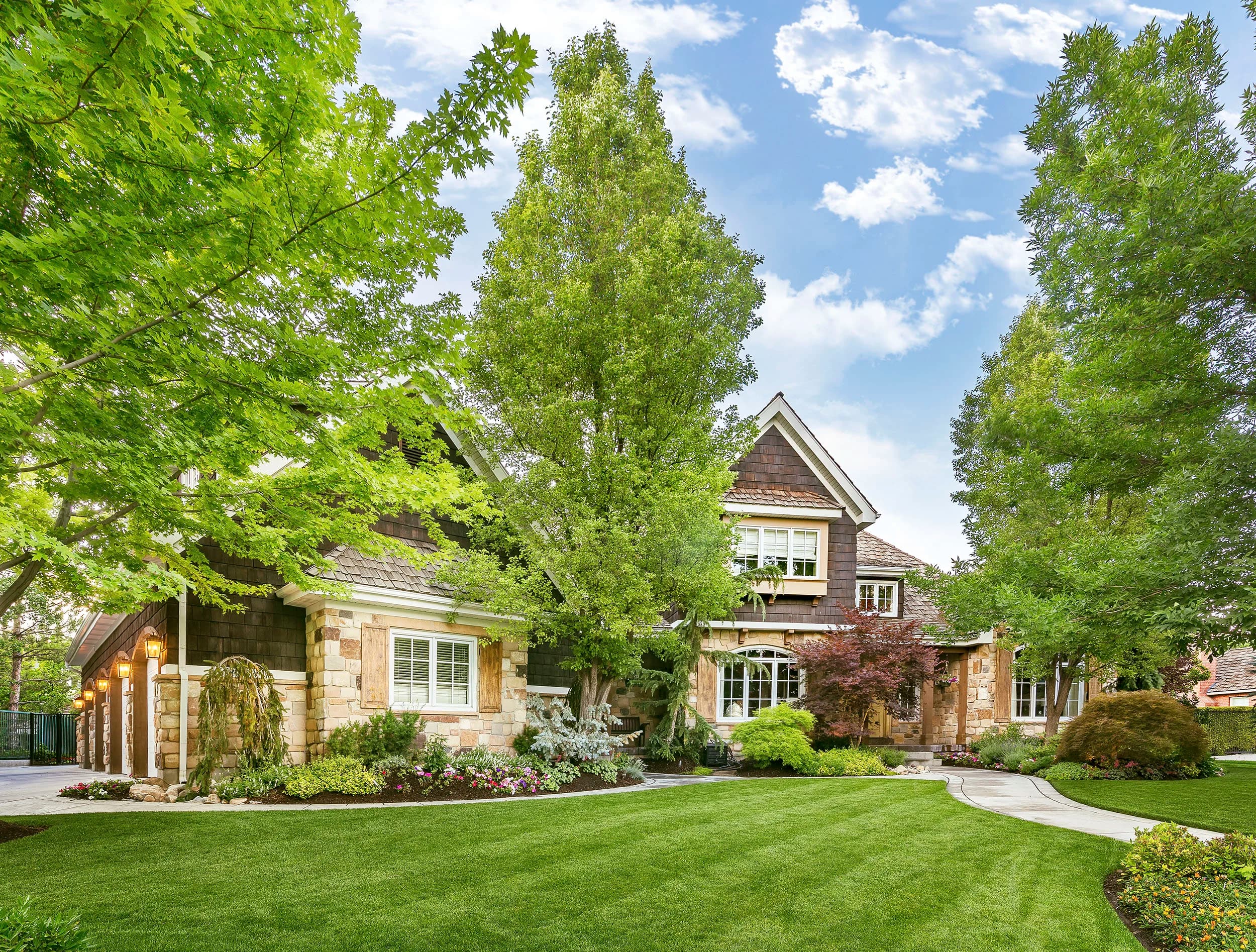 Big Rock Tudor-style estate with stone foundation, layered landscape beds, and a mature canopy of trees in Holladay, Utah