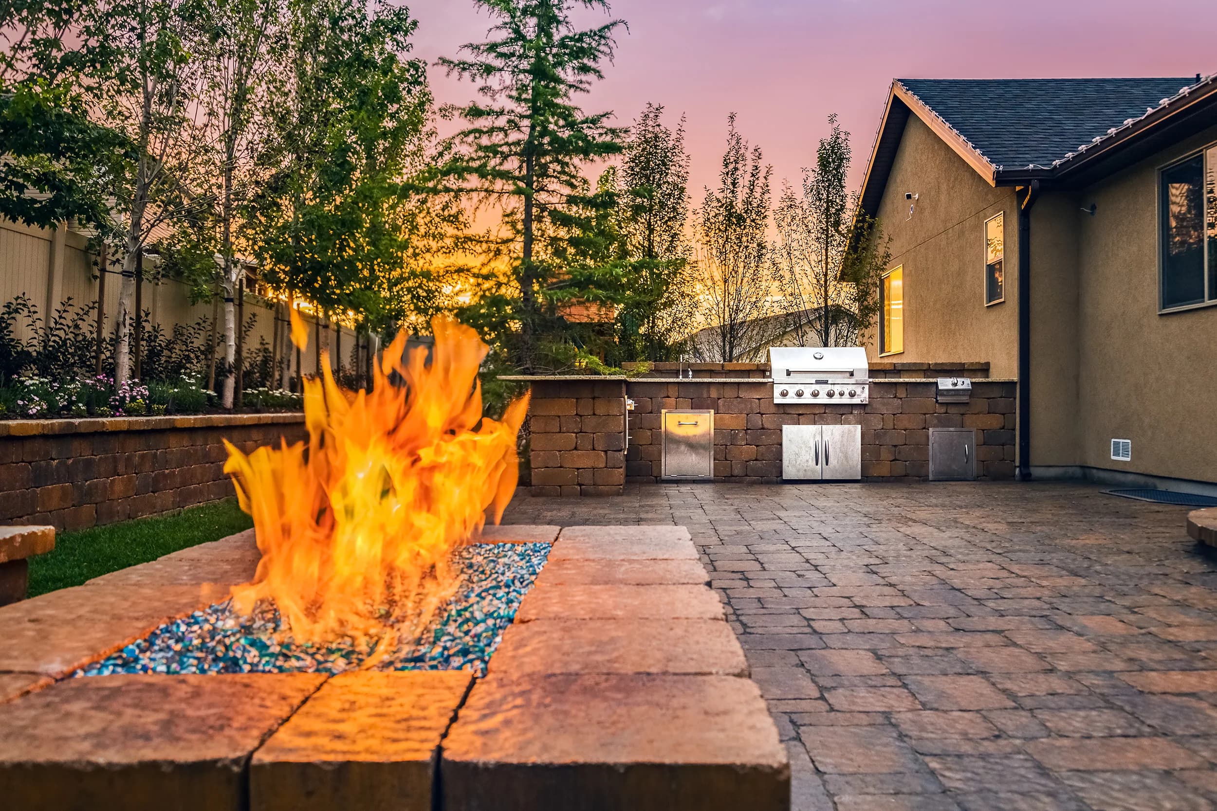 Twilight outdoor entertaining patio with stone fire pit, stainless built-in grill, and pink Wasatch sunset at Vintage Estates in Provo, Utah